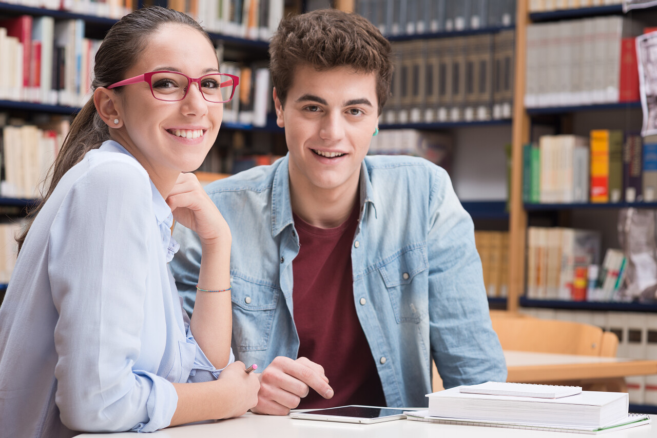 可爱的女学生戴着眼镜和一个朋友一起在图书馆学习