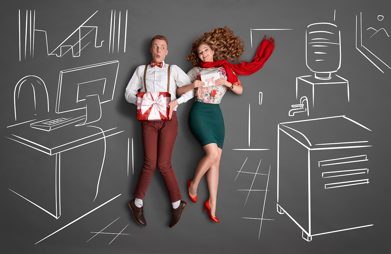 办公室里的恋情故事的概念。看着对方笑，分享礼物 图纸背景在上班的年轻夫妇.日记情人节