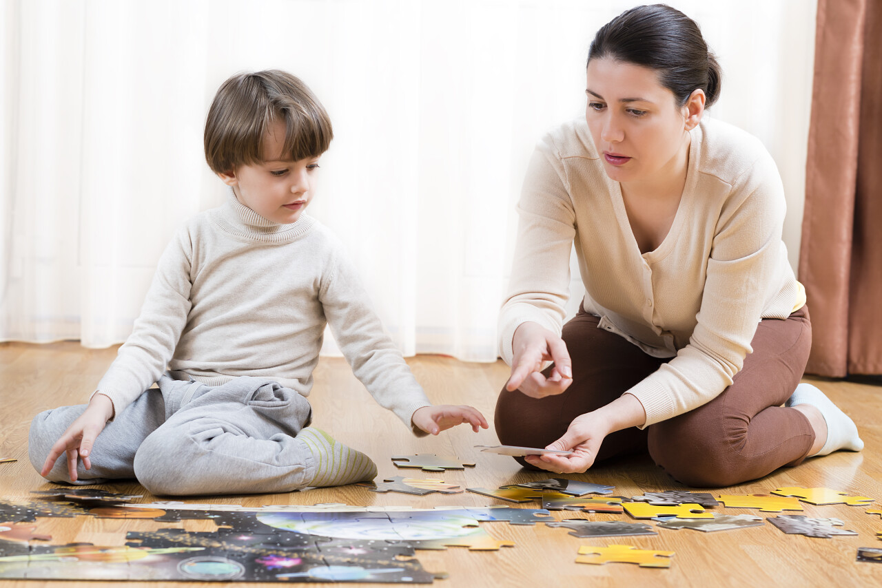 在家里孩子正在被他的母亲帮助组织拼图困扰