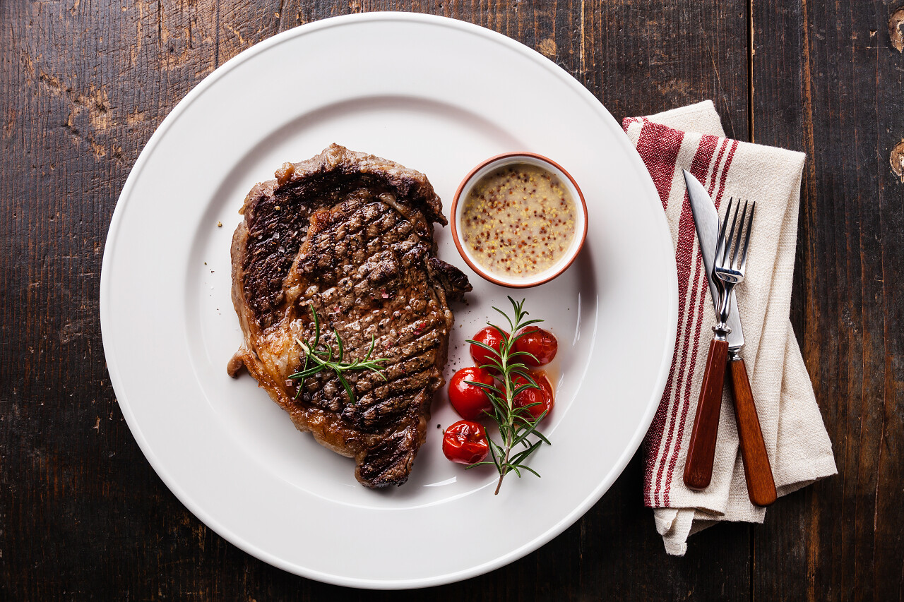 白色盘子里的烤牛肉牛排与樱桃西红柿西餐牛排