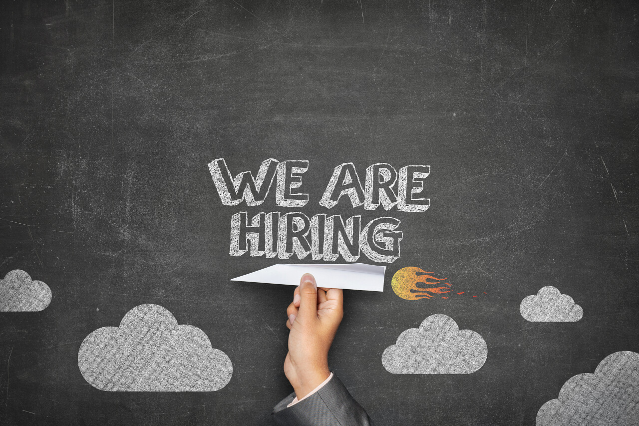 灰色背景黑板前商人手拿着纸飞机宣传招聘