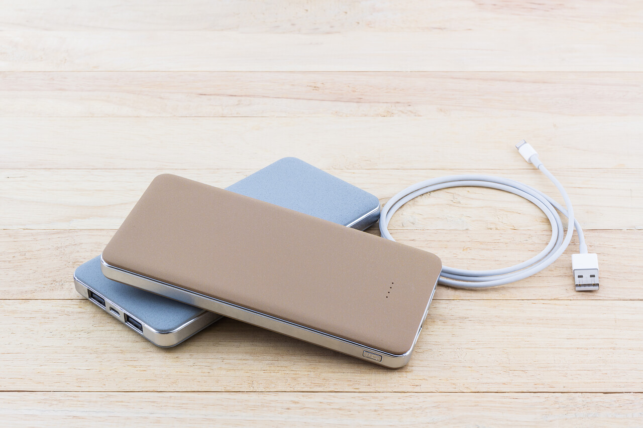 褐色木质桌面上电力银行智能手机和USB电缆