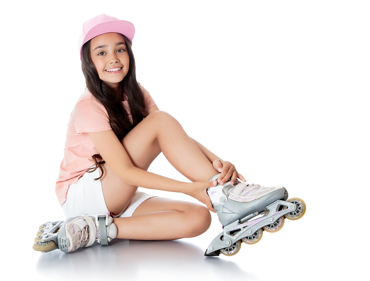 白色背景上分离坐着白色短裤和粉红色t恤脚穿旱冰鞋迷人的黑发女孩