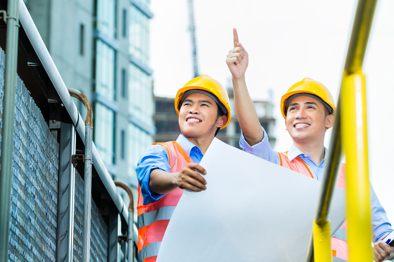 安全生产培训安全生产月两个建筑工人穿着工作服带着安全帽在规划蓝图