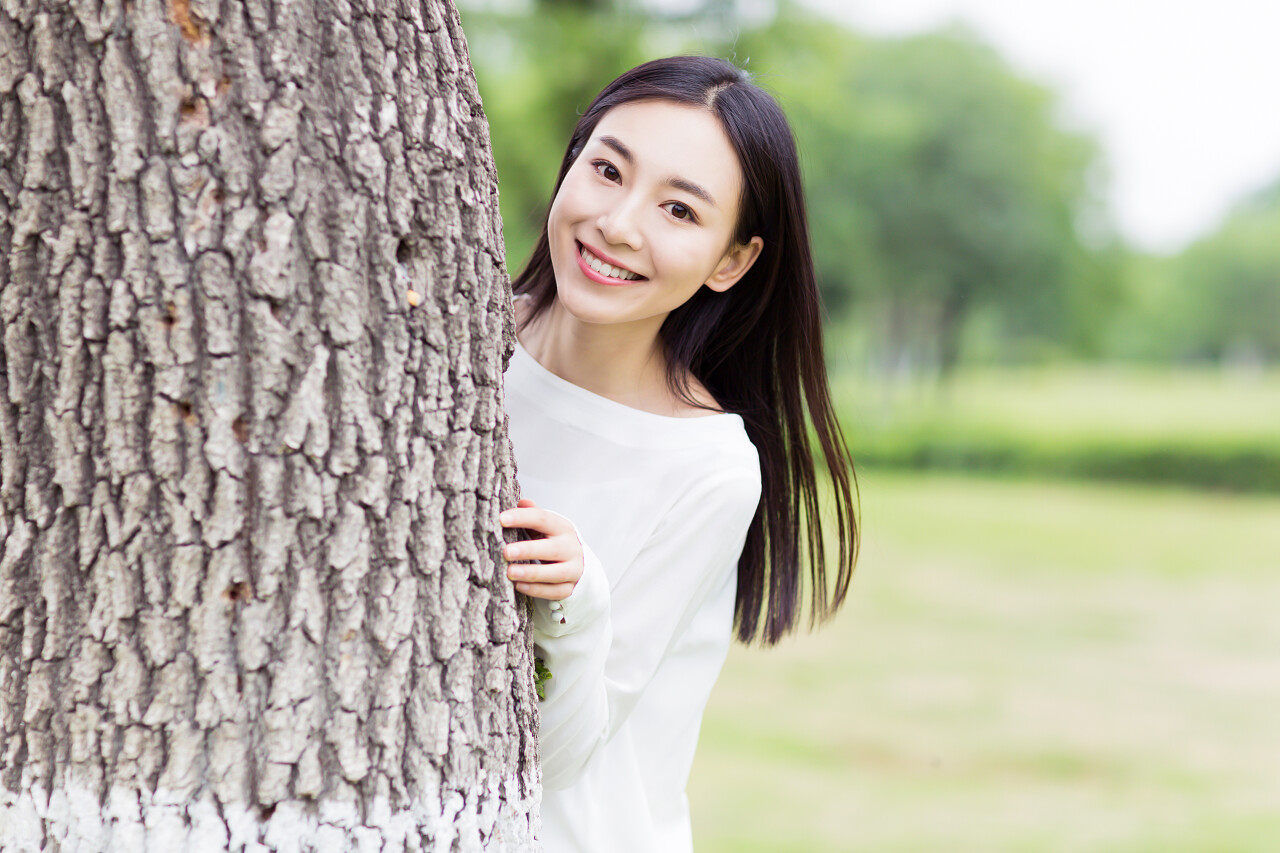 漂亮活泼的女孩躲在树后面捉迷藏