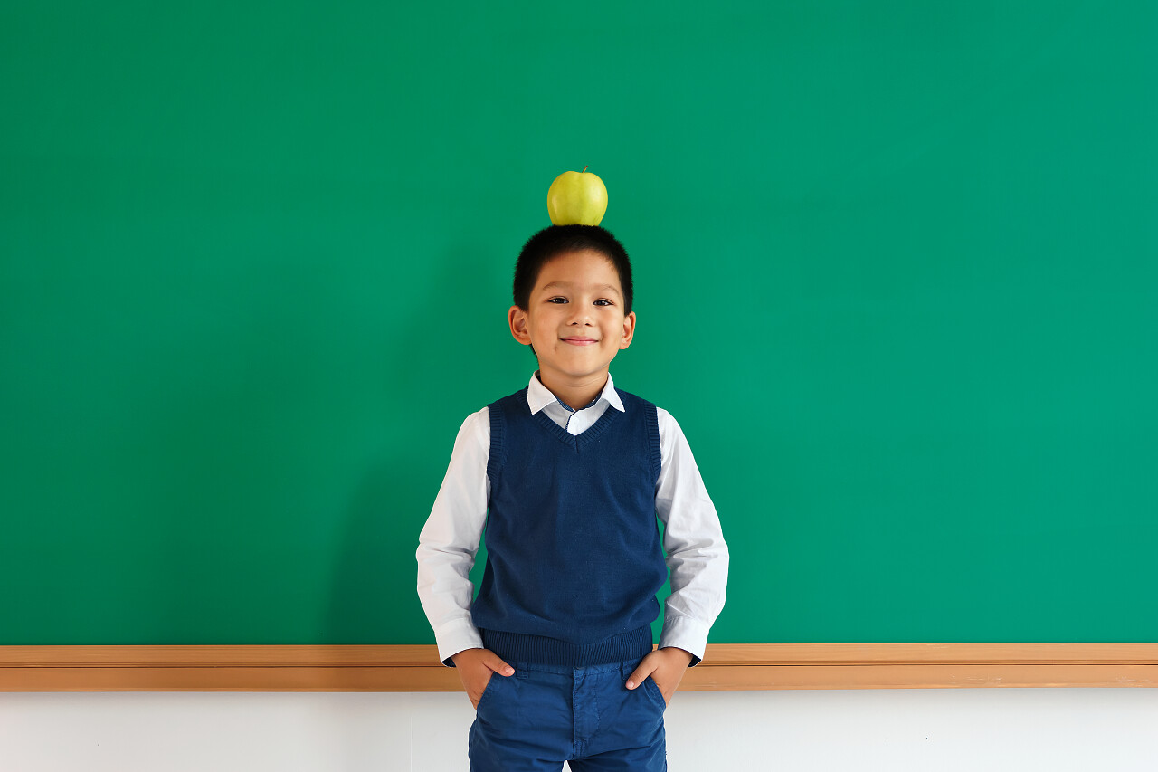 男生手插口袋里 同时平衡在他头上的苹果微笑的小孩