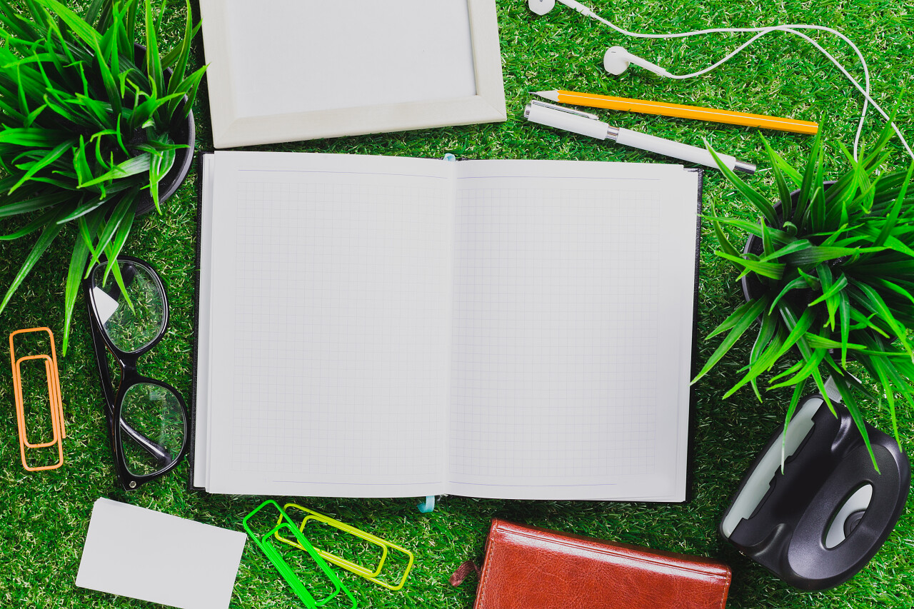 空白的笔记本、 手机和耳机在绿色草地上