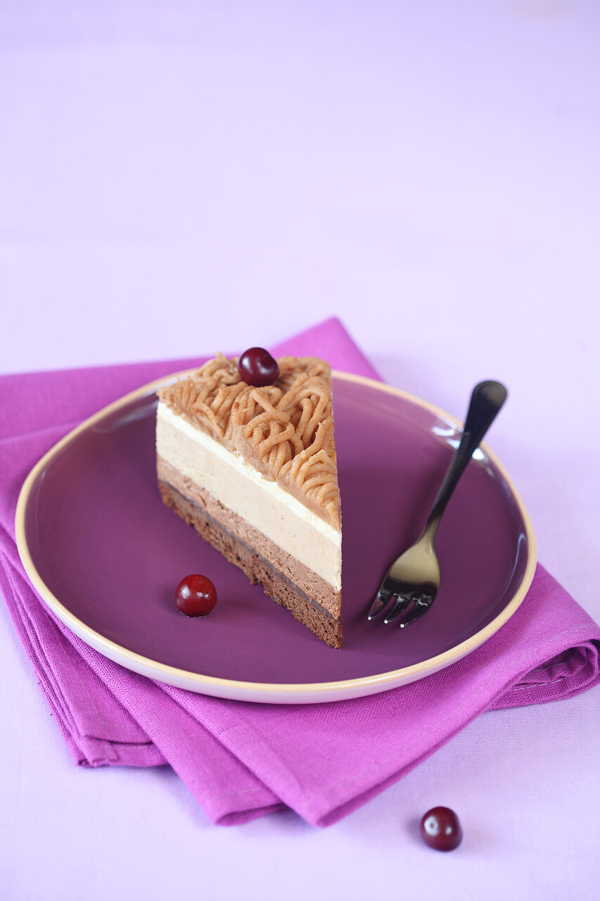 板栗多层慕斯蛋糕在明亮的紫色板和餐巾，浅紫色背景上的一块.