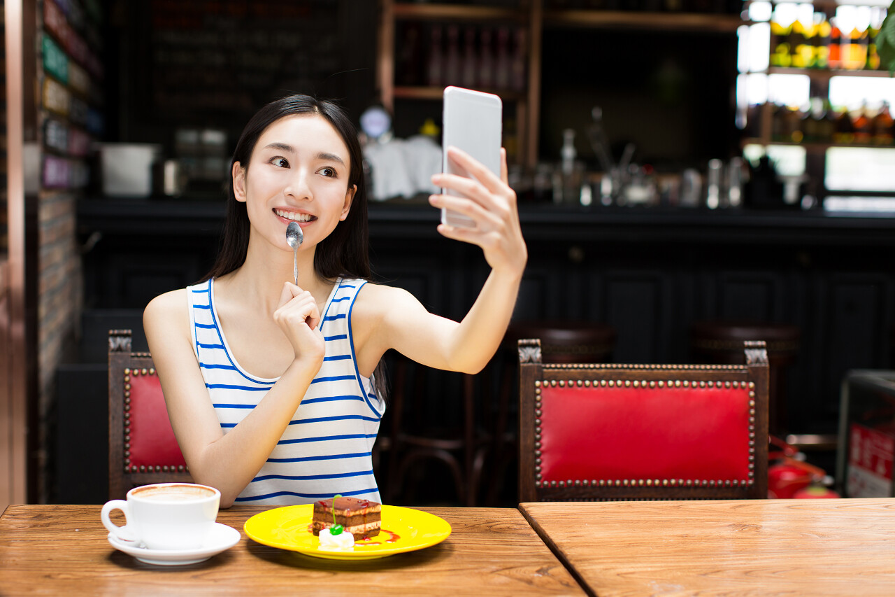 微笑着年轻的中国女子捧着电话和咖啡的自拍