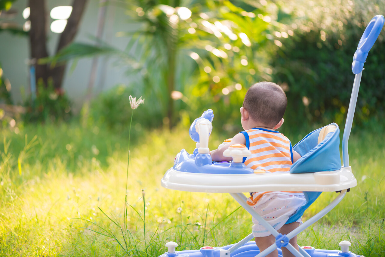 植物背景上坐婴儿学步车的亚洲可爱小宝宝