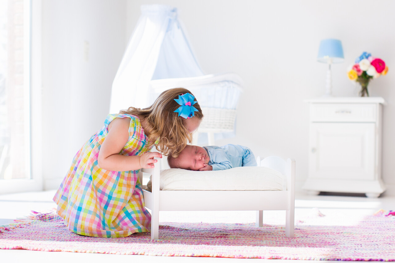 在白色苗圃玩具床上可爱的小女孩接吻新生弟弟