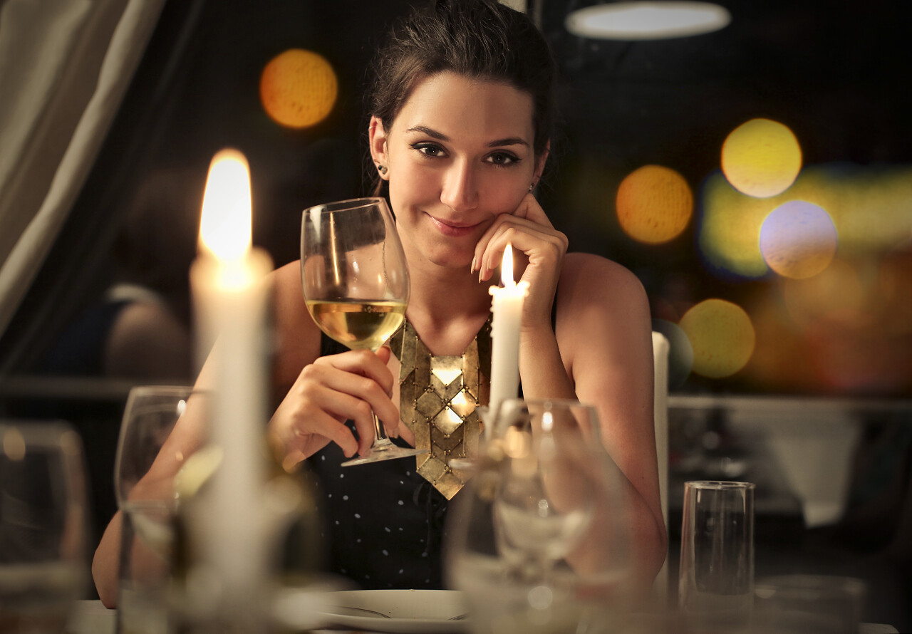 优雅的女人坐在餐桌旁拿着一杯白葡萄酒