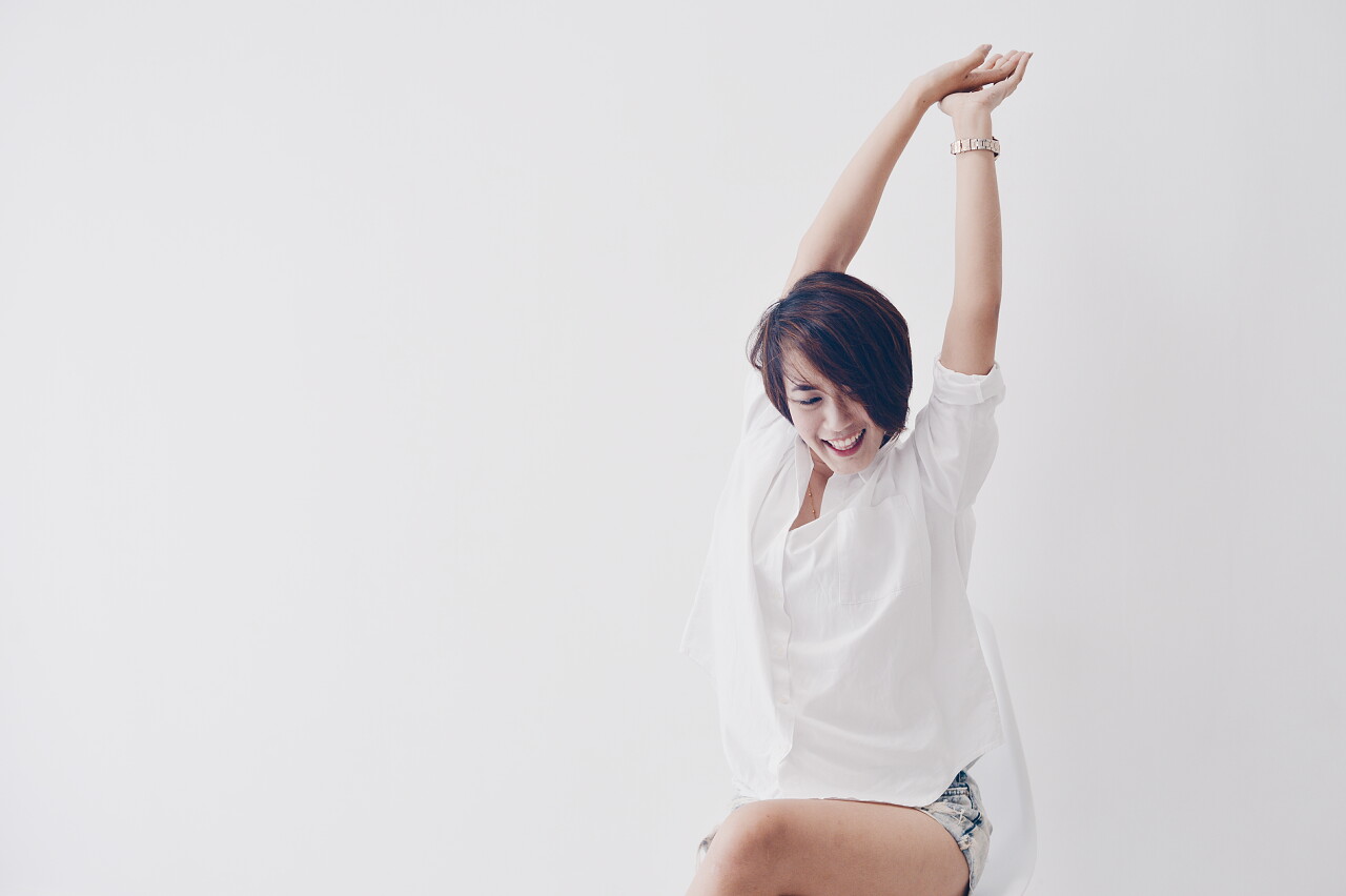 白色墙壁前伸着懒腰的年轻女性疲劳