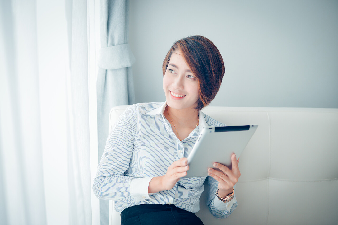 一位商业女性坐在家里的沙发上使用平板电脑