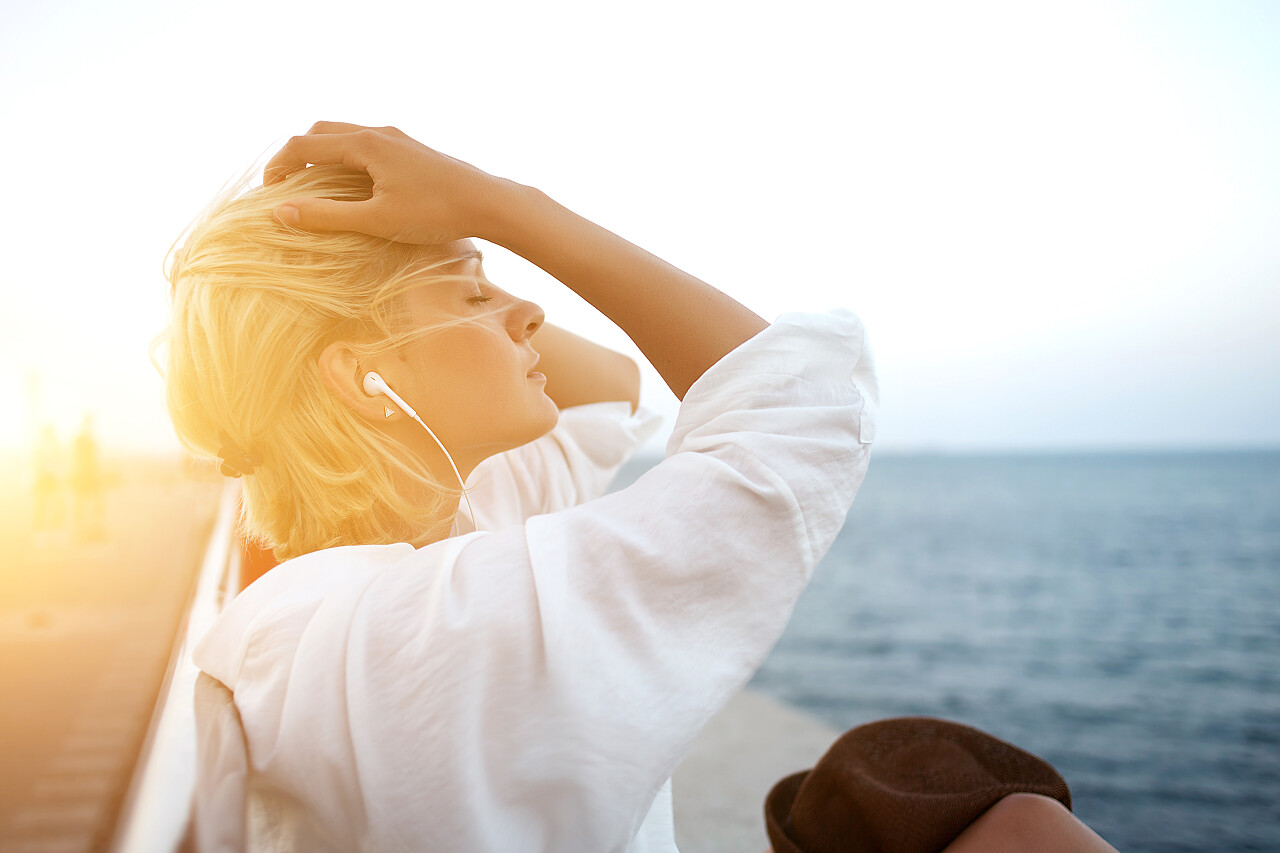 年轻迷人的女人坐在海边聆听最喜欢的音乐放松