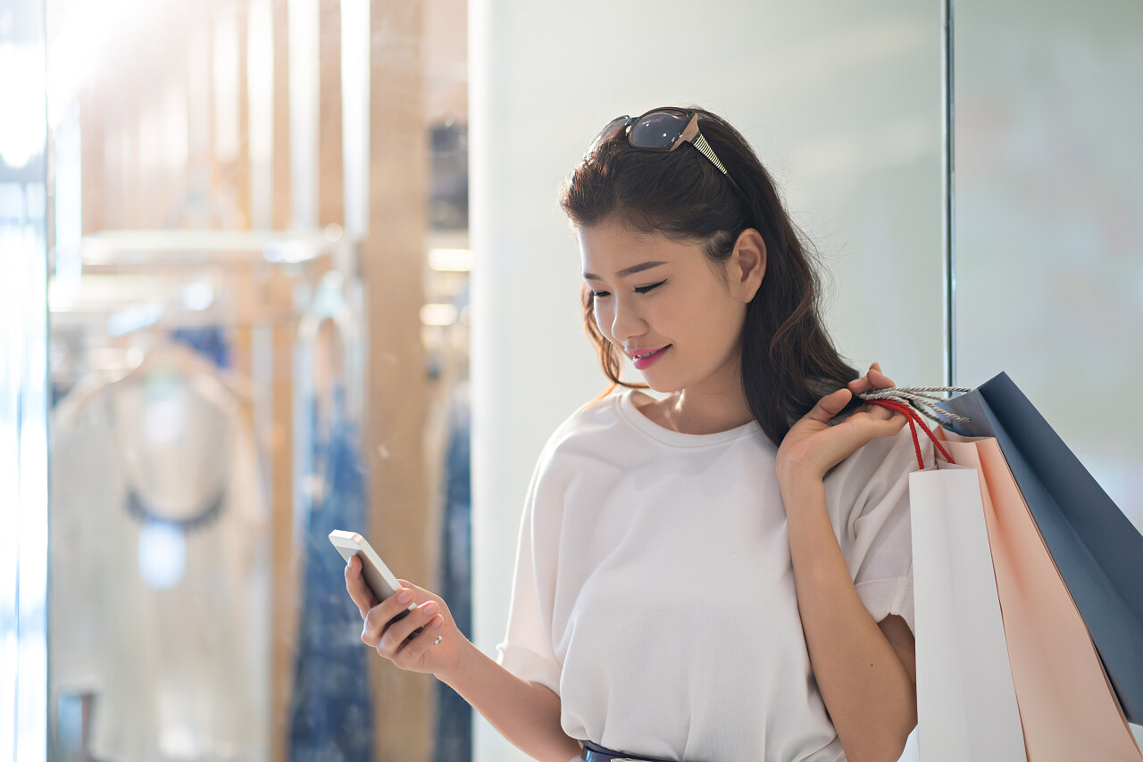 拿着纸袋微笑的漂亮女人阅读电话上消息的肖像