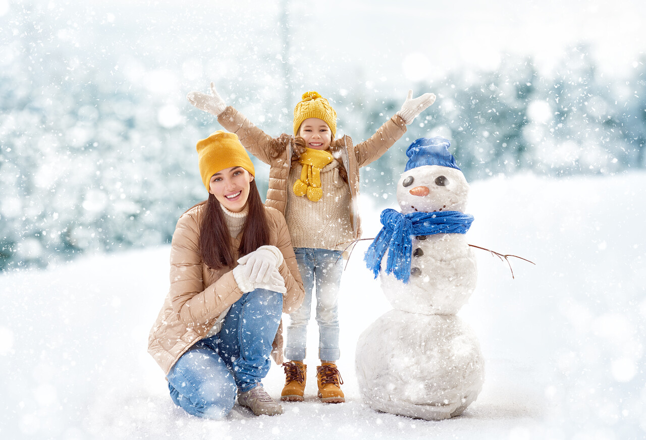 一位美丽的女人在雪堆里和他的孩子堆雪人