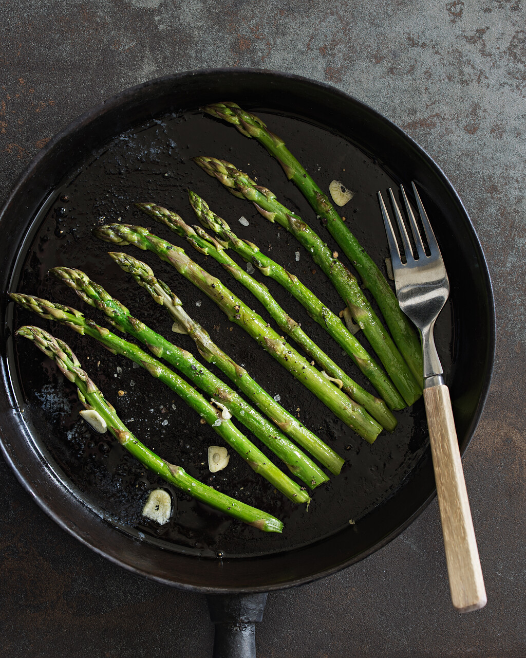灰色背景下用叉子食用平底锅上蒜茸炒芦笋