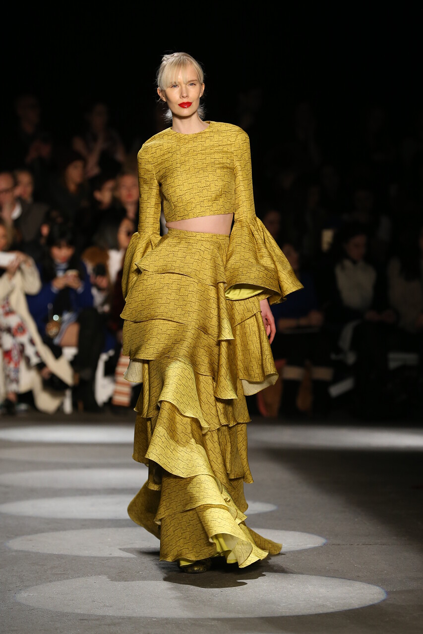 位色背景下一名模特穿着时尚的服装走在跑道上