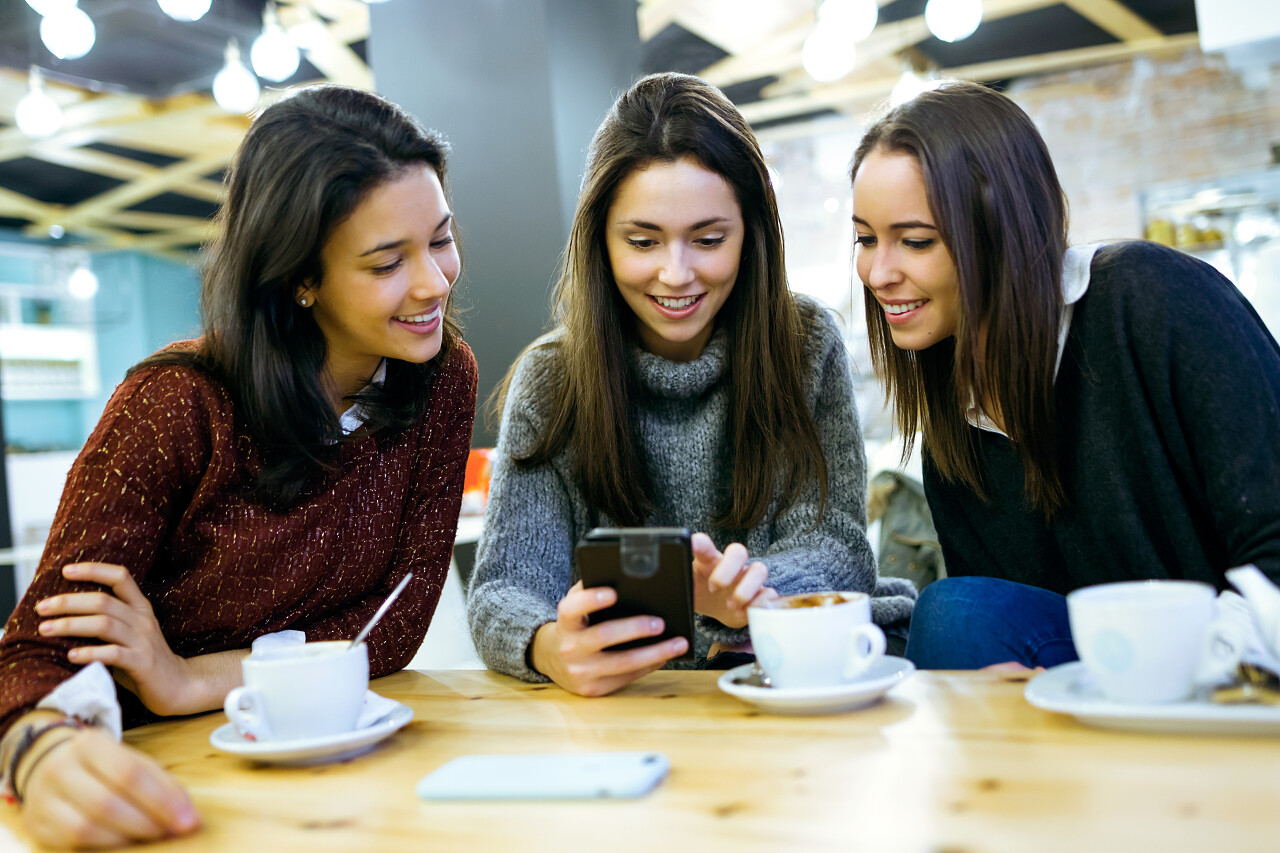 咖啡店使用移动电话的三个年轻漂亮女性的肖像