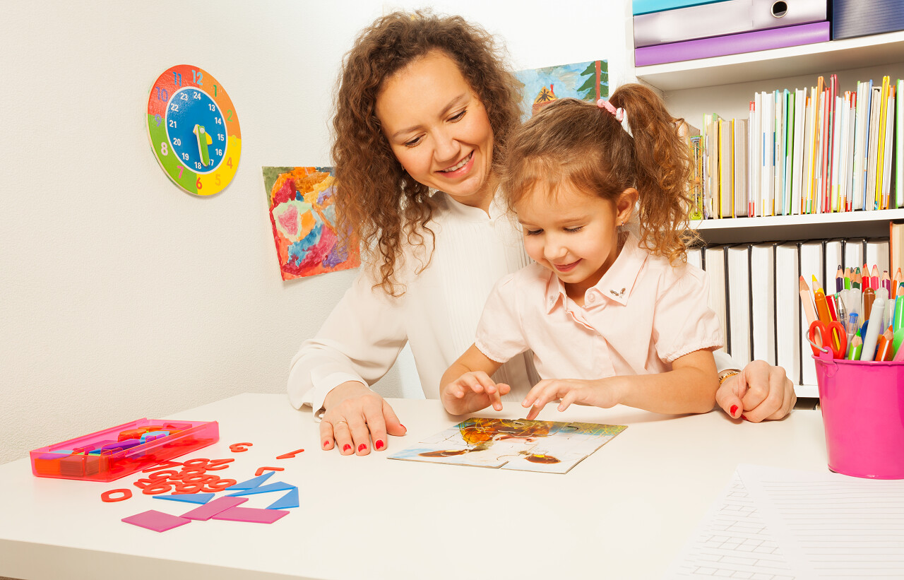 女学生和她的老师在教室的课桌上拼接拼图游戏