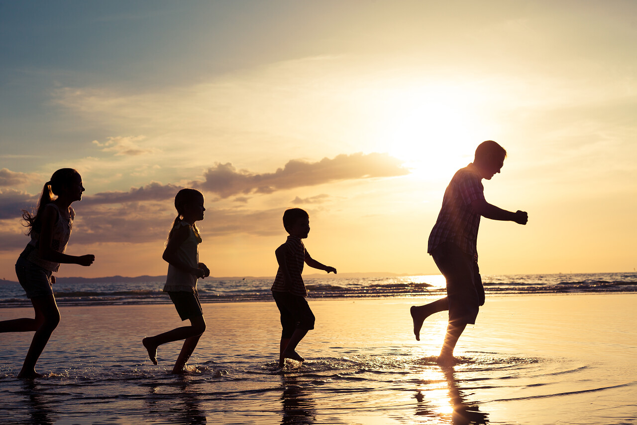 日落时在海滩上玩的父亲和孩子们