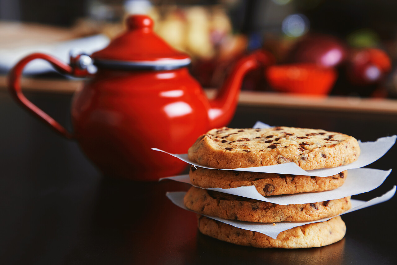 美味脆脆的自制饼干和红色复古茶壶热饮在黑桌上