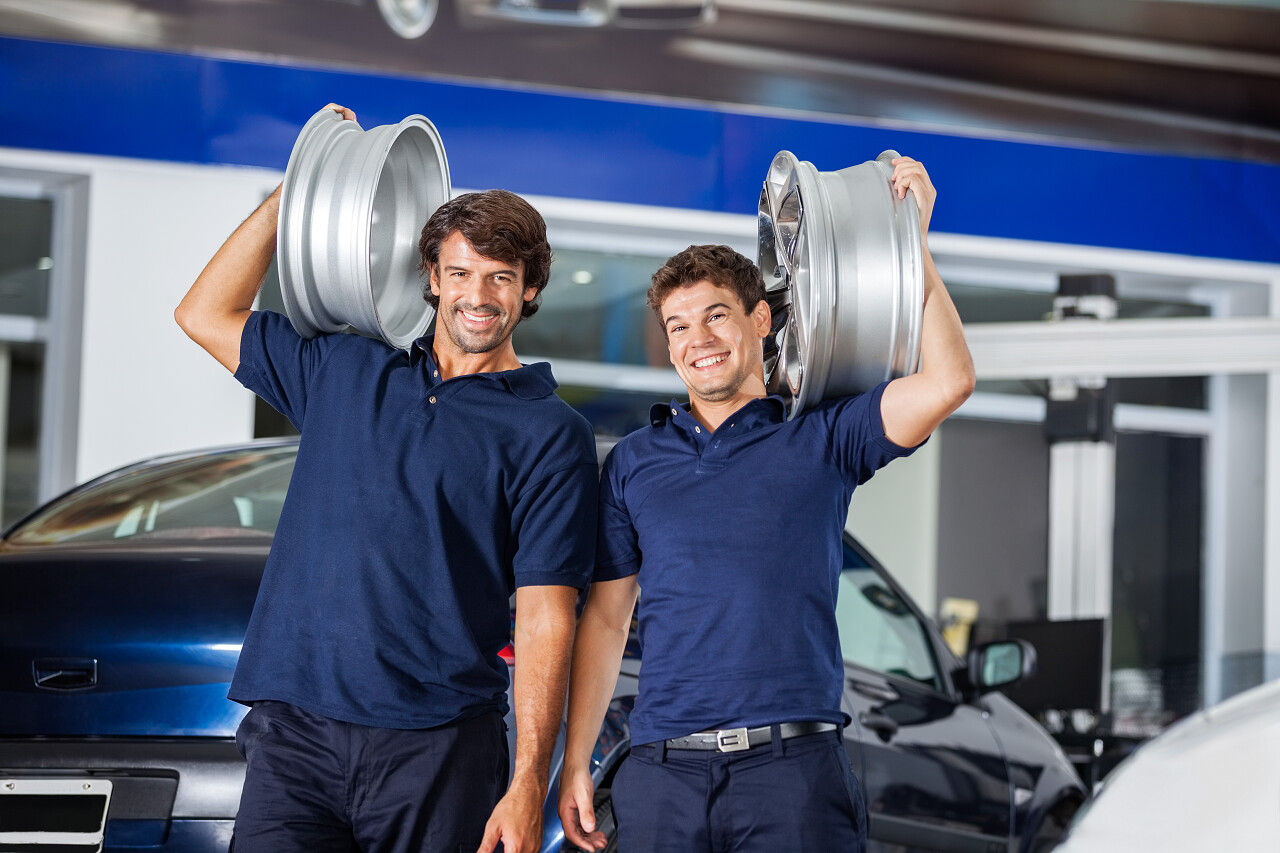 快乐的技术人员肩膀上携带金属合金在汽车维修店的的照片