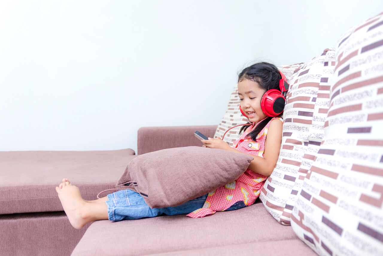 一位可爱的小女孩正躺在沙发上使用耳机听歌