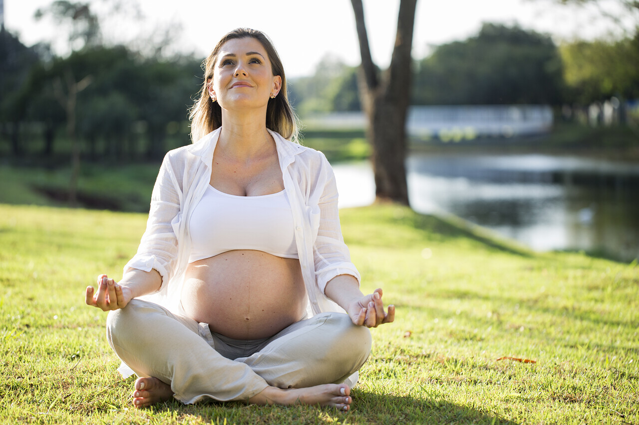 在公园里孕妇在日落时分坐在草坪上练瑜伽户外瑜伽