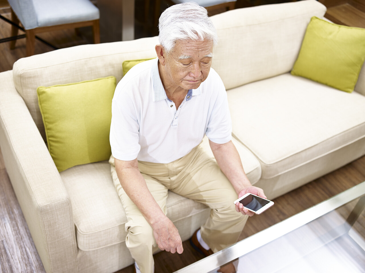 孤独的亚洲高级手坐在沙发上看手机