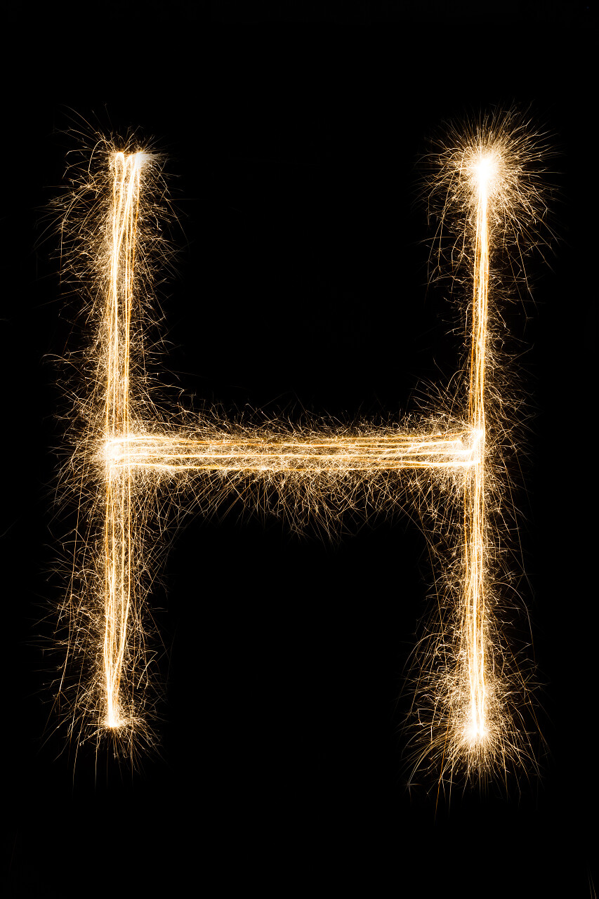 燃烧的火花在黑色背景上的英文字母 H