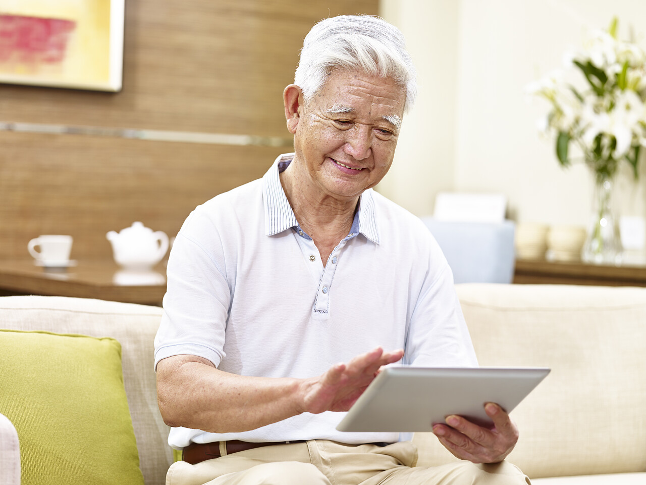 一位老年人微笑着坐在沙发上使用平板电脑放松微笑的老人