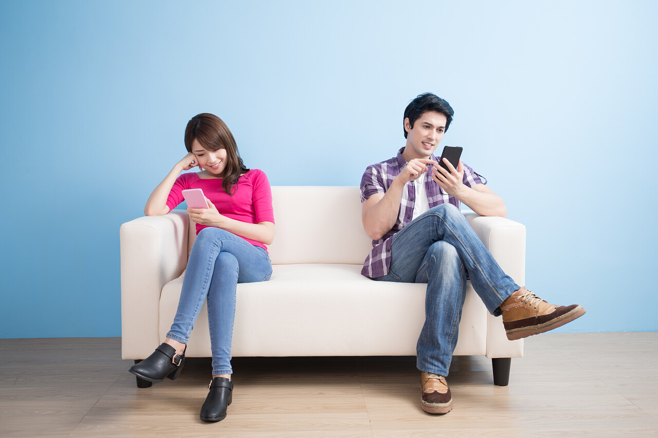 蓝色背景下正坐在沙发上的年轻的夫妇