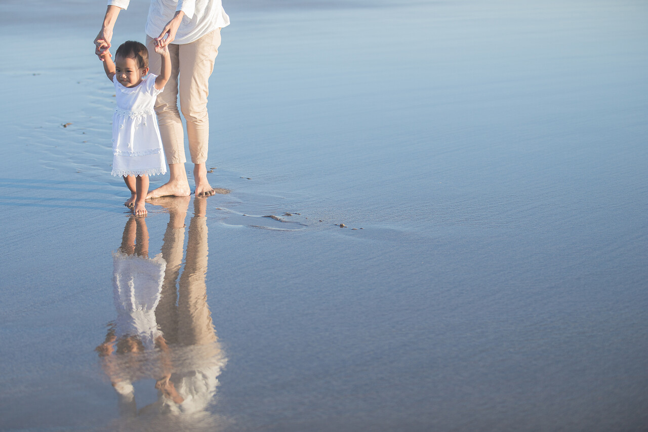 在沙滩上教婴儿学走路的母亲