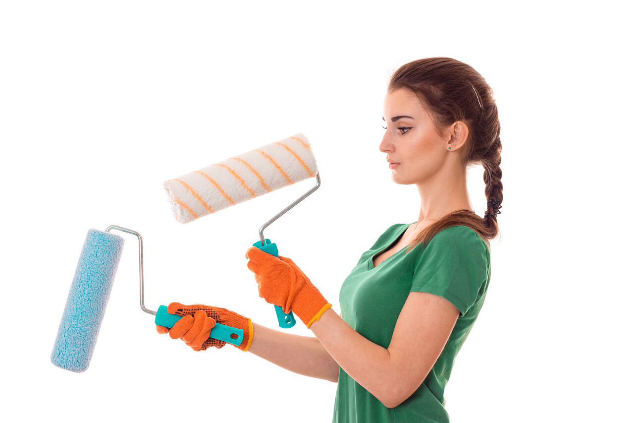 年轻的黑发女人穿制服用涂料滚子在她手里装修