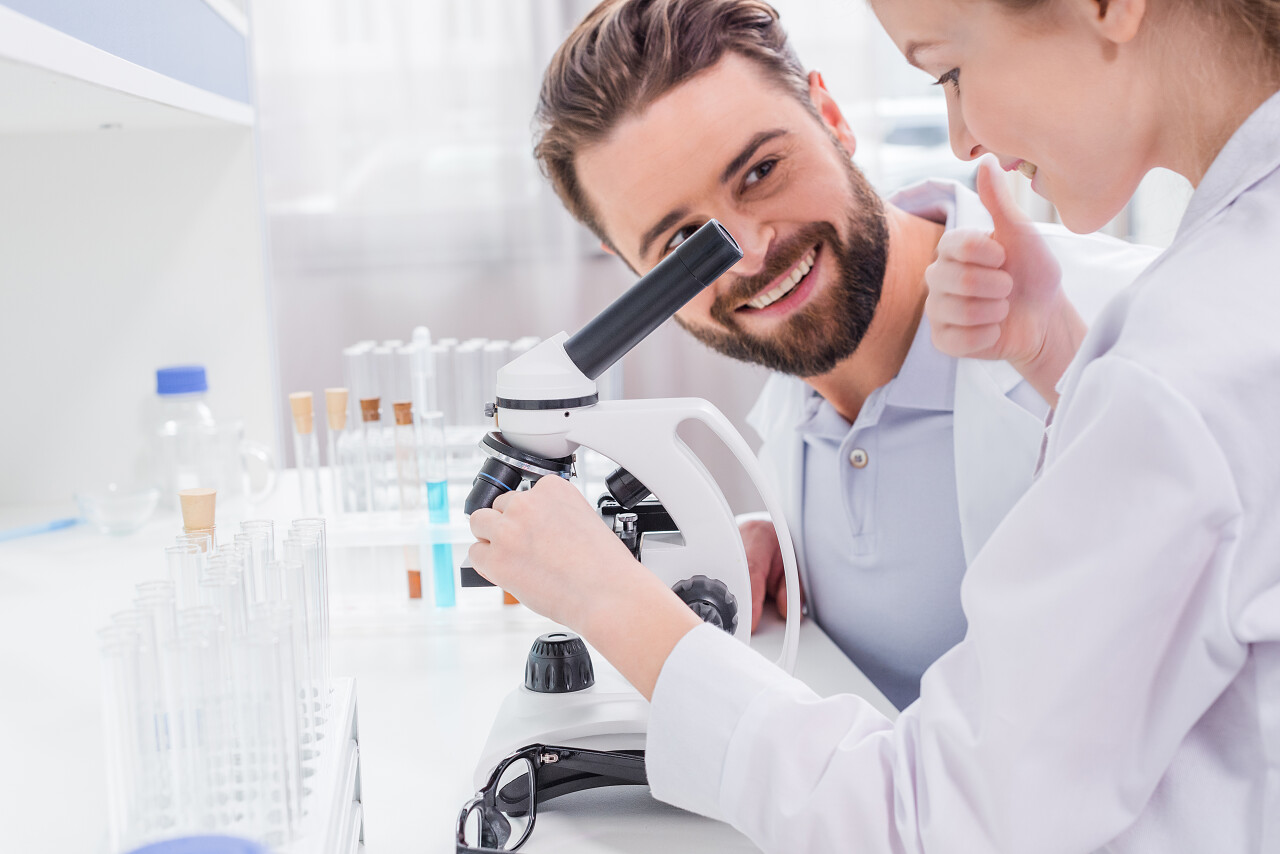 微笑着胡子的老师看着学生用显微镜在实验室里工作