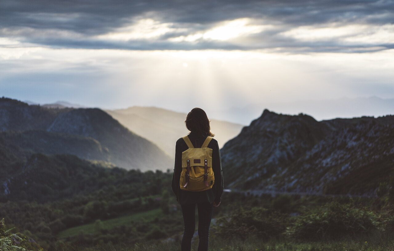 时髦的年轻女孩与享受日落在有雾的山峰上的明亮背包努力坚持不懈克服困难