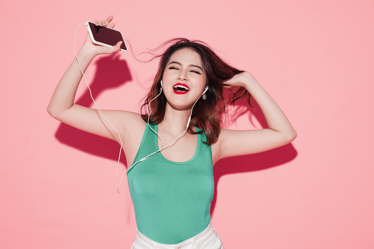 美丽的亚洲女孩在粉红色的背景上唱歌和跳舞