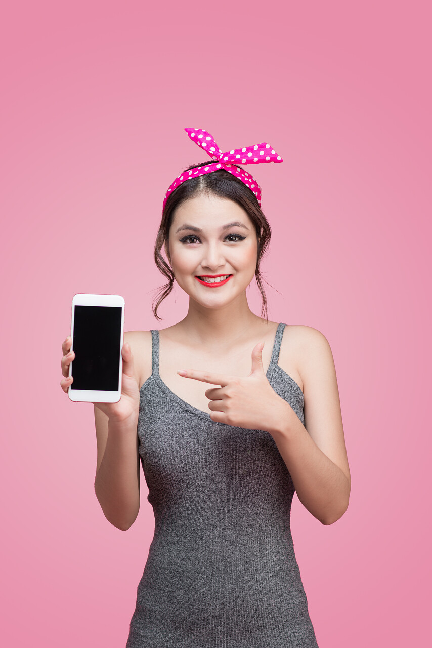 在粉红色的背景上亚洲女孩拿着移动电话