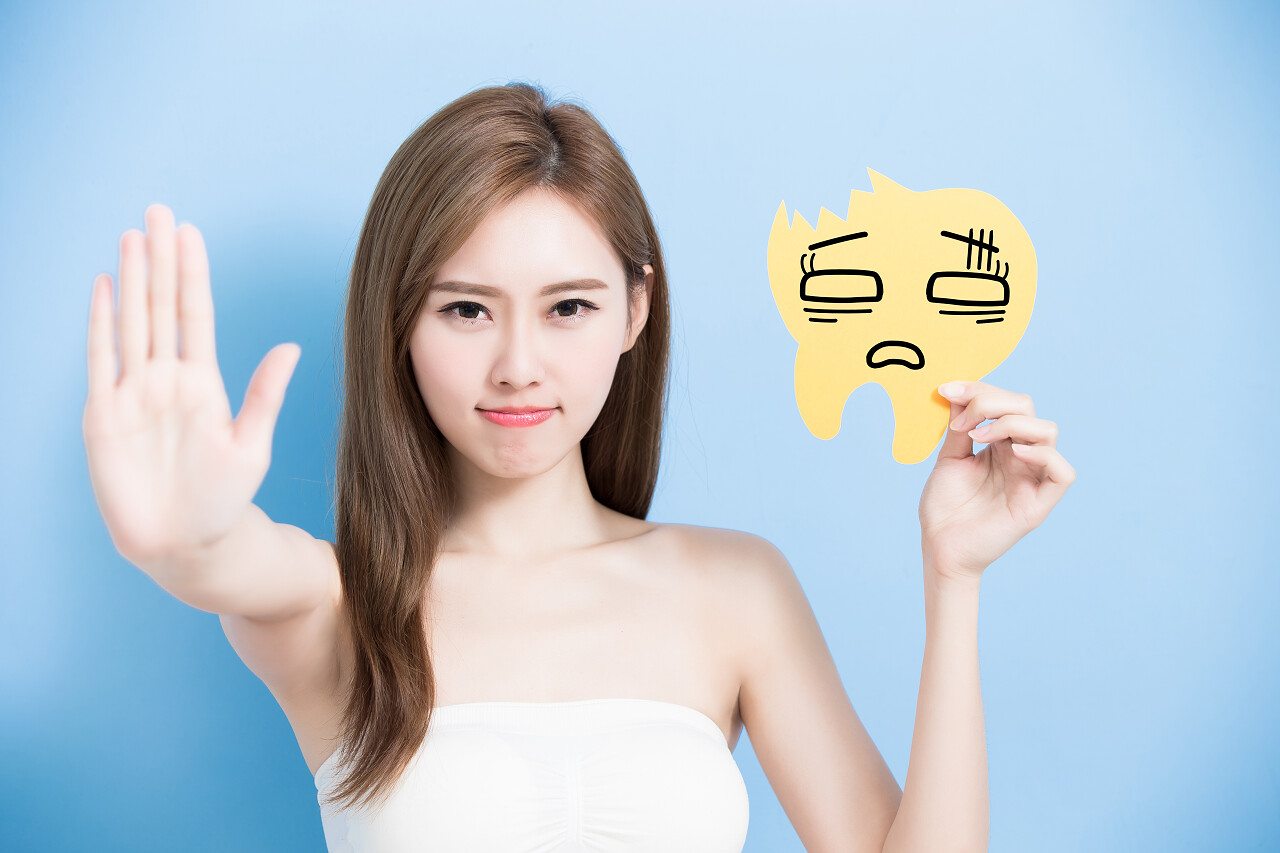 在蓝色背景上拿着牙齿广告牌并做停止手势的女人