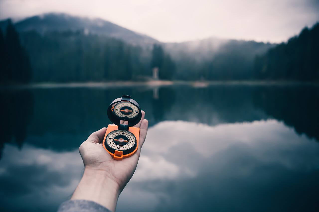 男手拿黄色的旧学校指南针上高山湖泊和迷雾森林