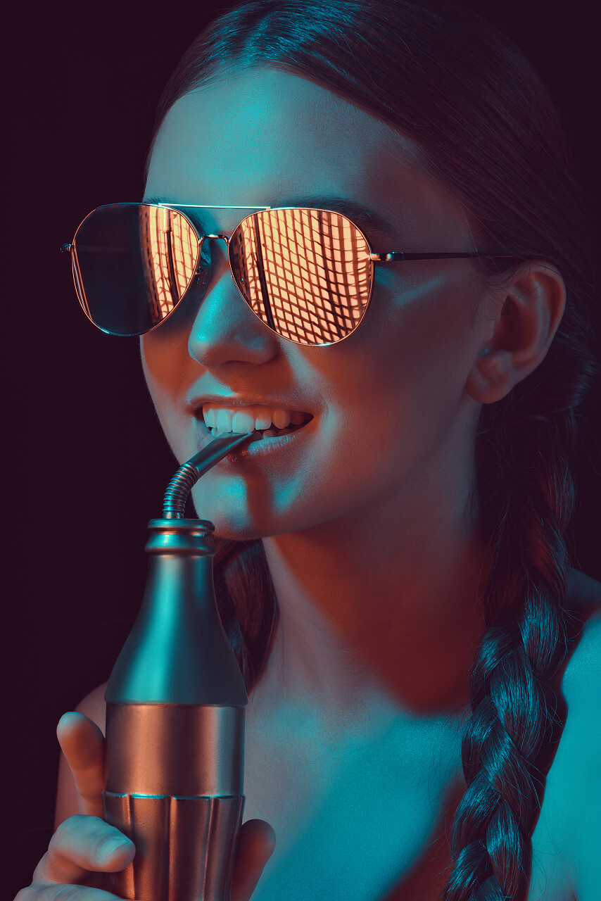 微笑的女士太阳镜从用稻草瓶水喝苏打水