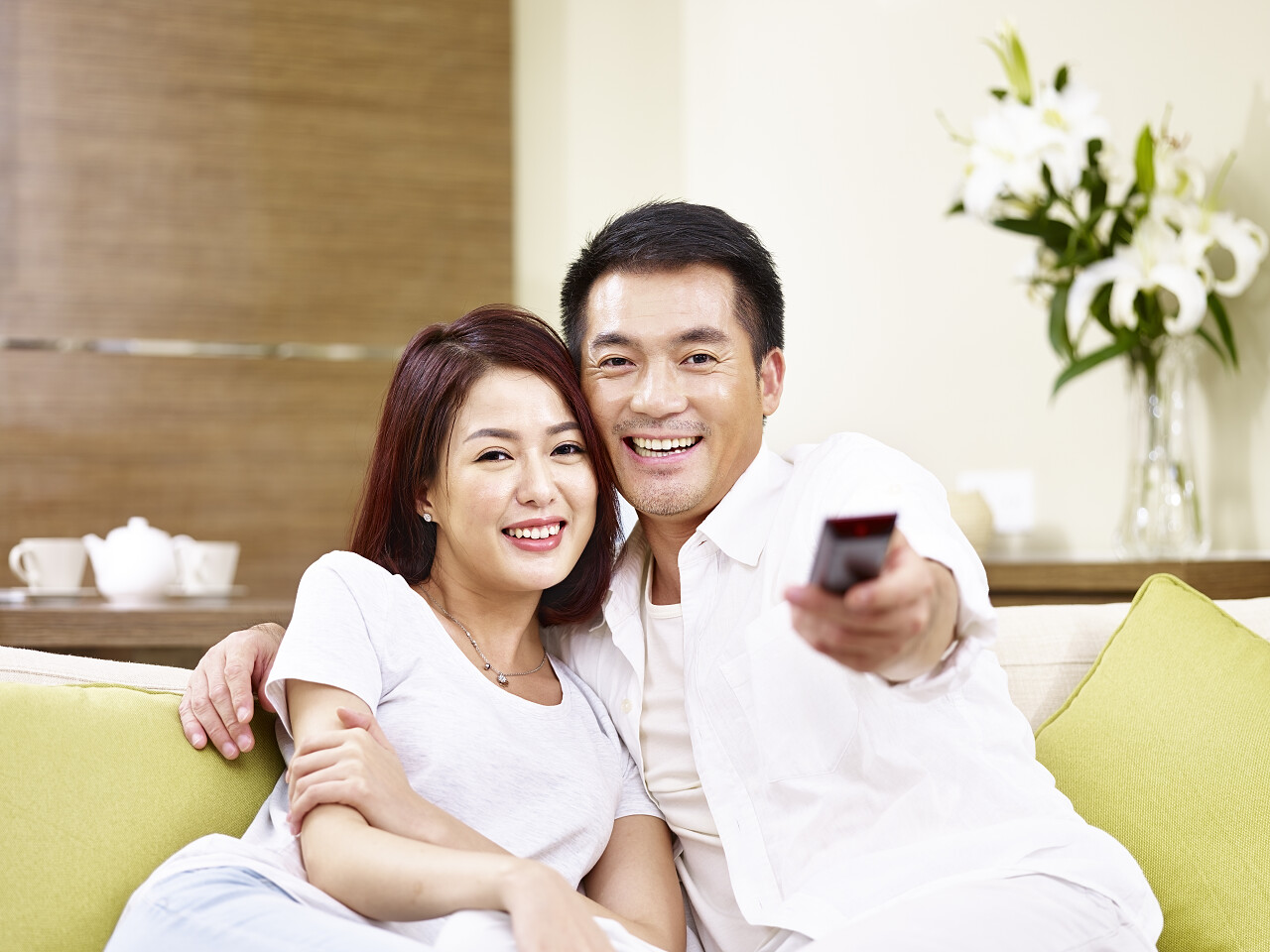 坐在沙发上切换频道使用远程控制看电视的时候对亚洲年轻夫妇.