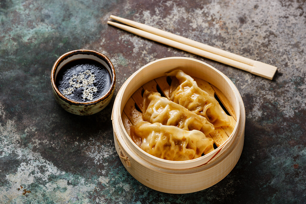 蒸饺煎饺在竹蒸笼用筷子和酱油上金属背景