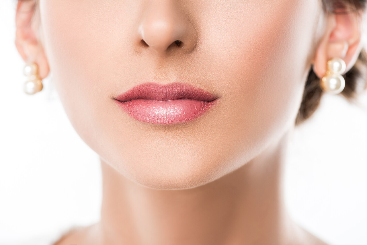 裁剪的应用的粉色唇膏嘴唇上的美丽女性面对镜头嘴唇纹唇美容