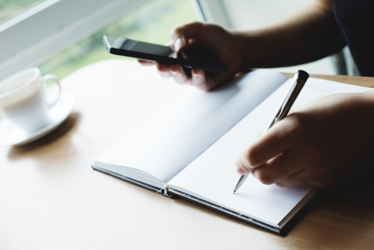 手持钢笔和使用手机的女性手部特写照片