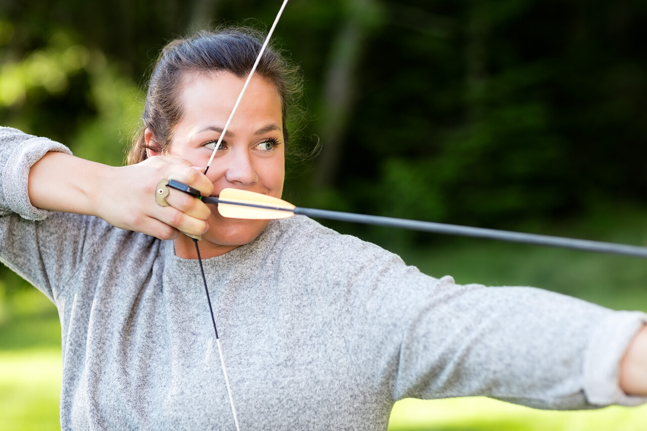 年轻女运动员用弓和箭在森林里