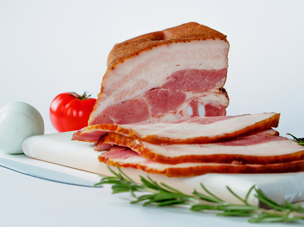 烟熏培根白切菜板用白色彩色西红柿和白色背景上的刀