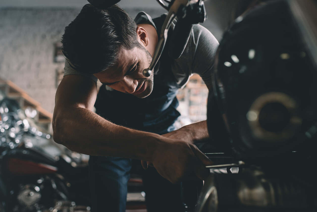 年轻英俊技工戴着护目镜在车间维修摩托车